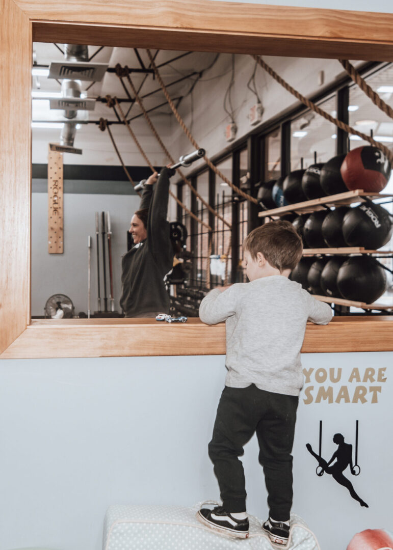 Toddler watching mom weightlift in gym.