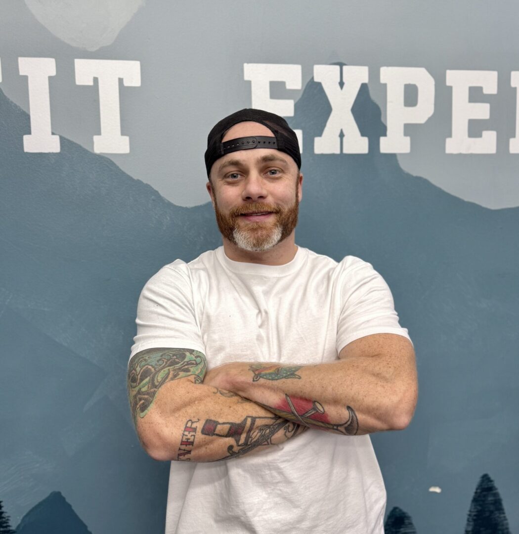 Man with tattoos, arms crossed, fitness expert.